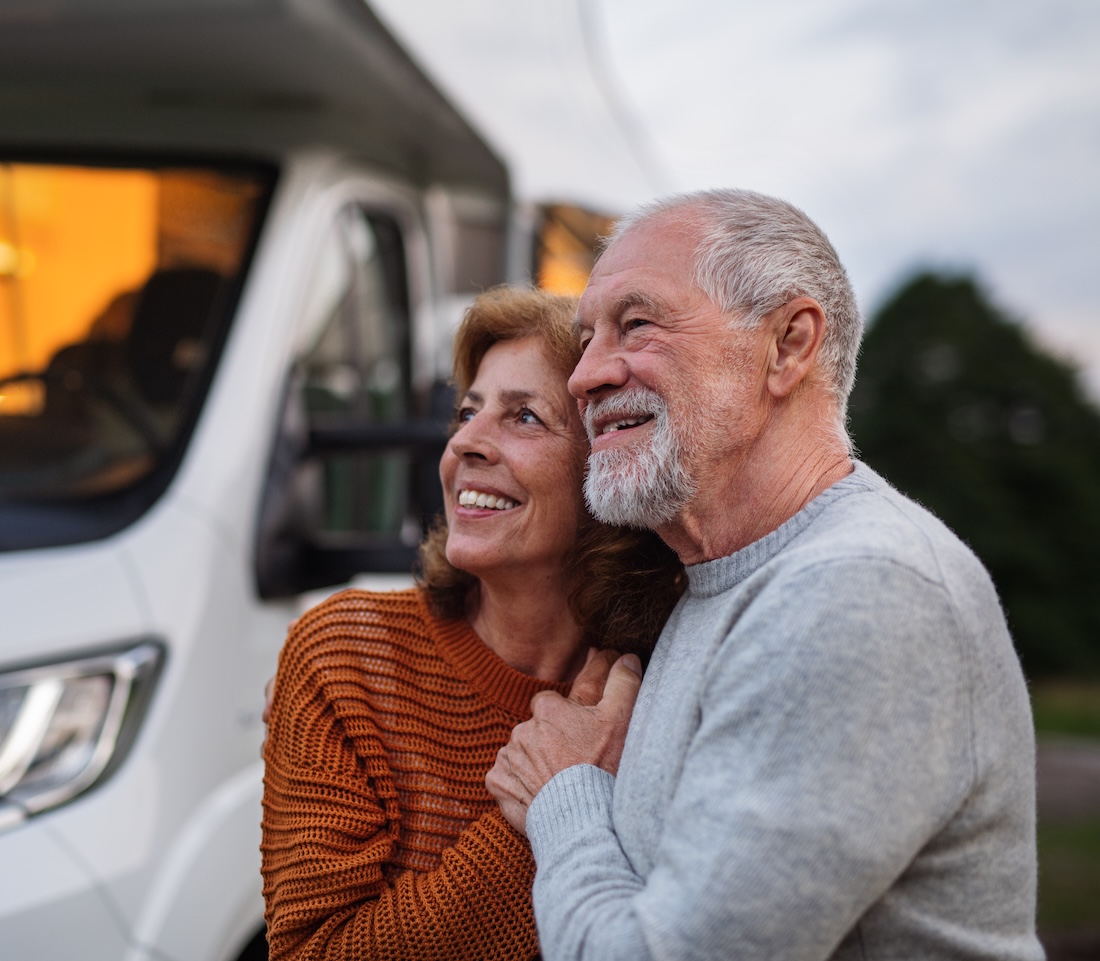 A senior couple standing and hugging outdoors at dusk, caravan holiday trip.